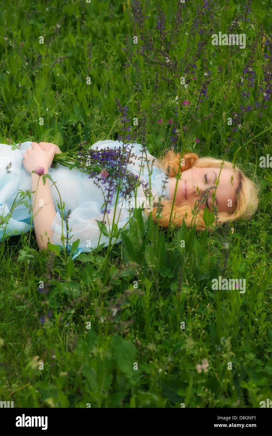 a blond girl, lying on a flower meadow and sleeping Stock Photo