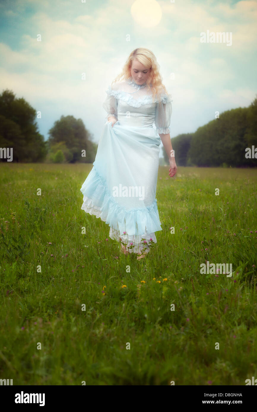 a blond girl in a vintage dress is walking on a meadow Stock Photo