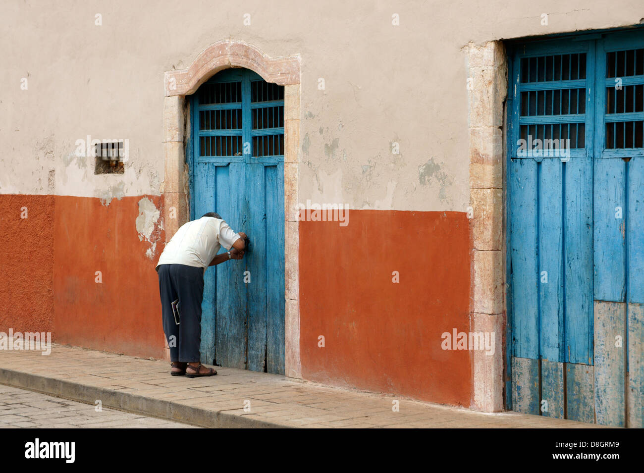 Man bending over to lock an old wooden door in Santa Elena, Yucatan, Mexico Stock Photo