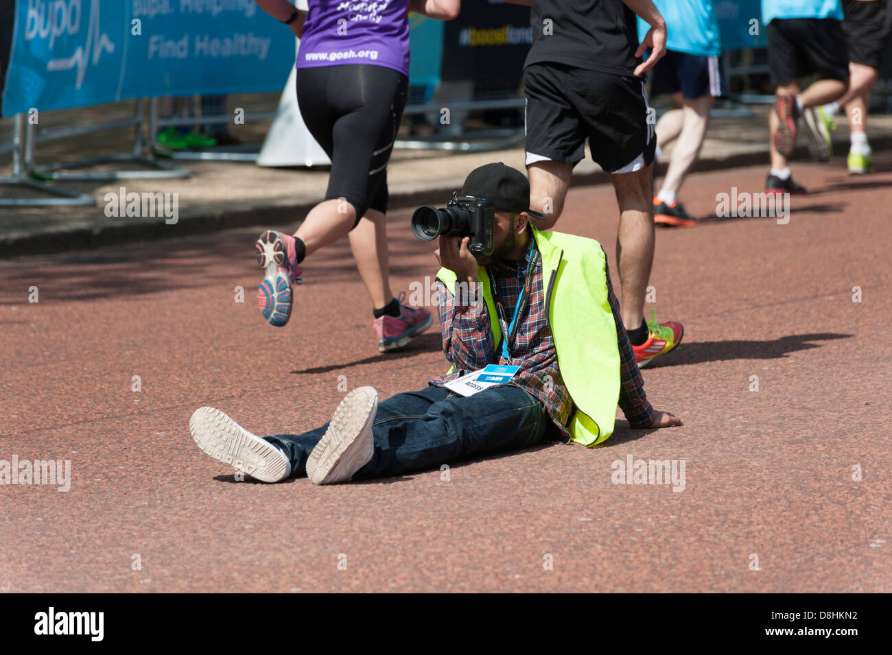 A marathon foto photographer taking photos at the BUPA London 10k run 2013, sitting in road with blurred runners passing him Stock Photo