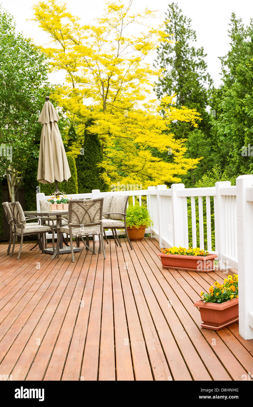 Vertical photo of a large outdoor natural cedar deck with patio furniture and bright yellow and green trees in background Stock Photo