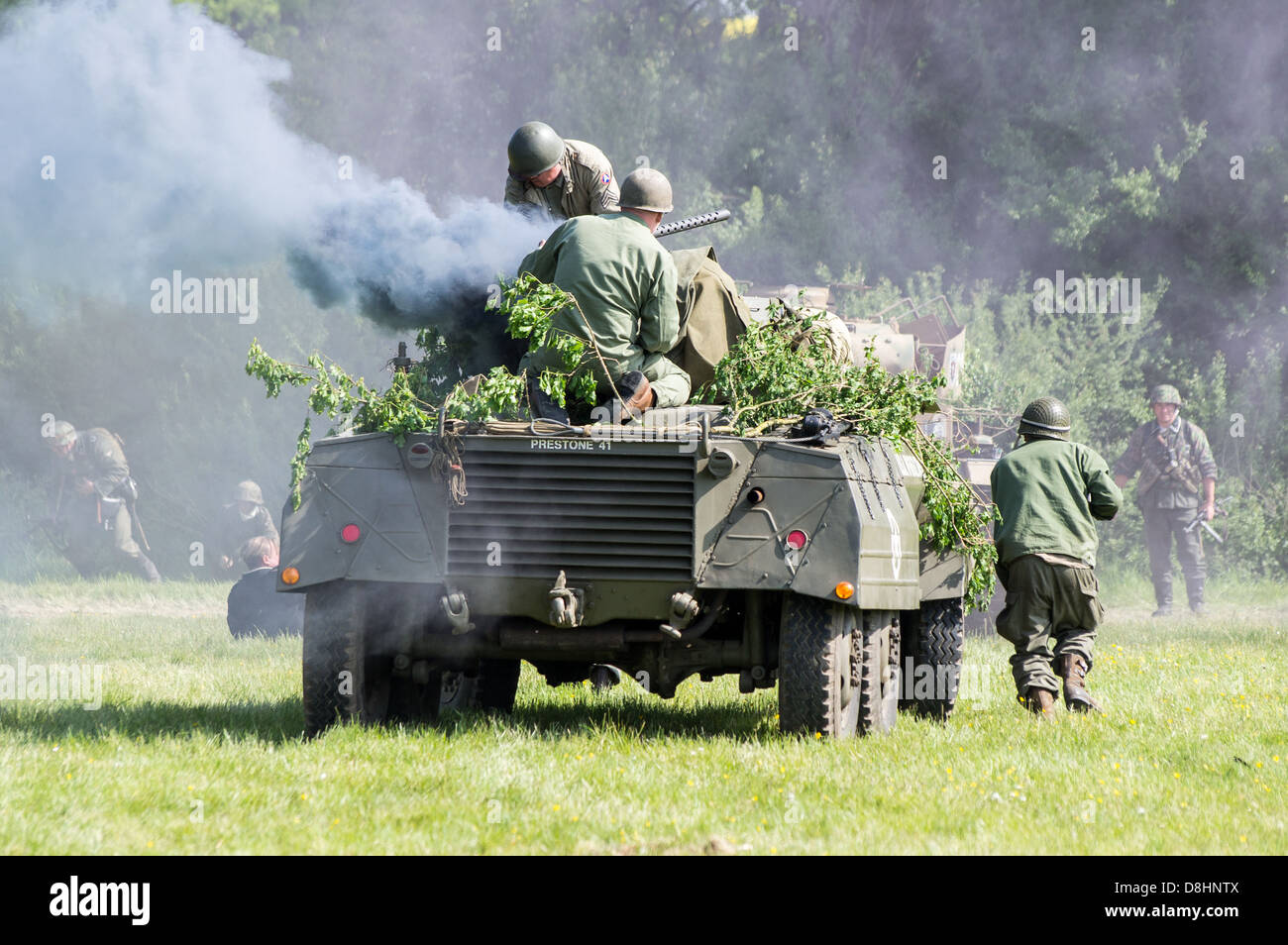 Overlord, D-Day re-enactment at Denmead 2013. American M8 Greyhound Armoured car advancing with troops with smoke pouring out. Stock Photo