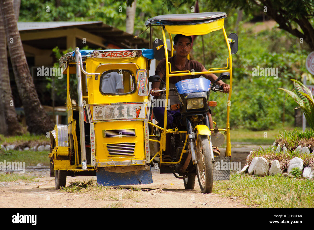 Asian man (Filipino) riding a yellow tricycle, motorbike with sidecar, on a tropical jungle road – Puerto Galera, Philippines Stock Photo