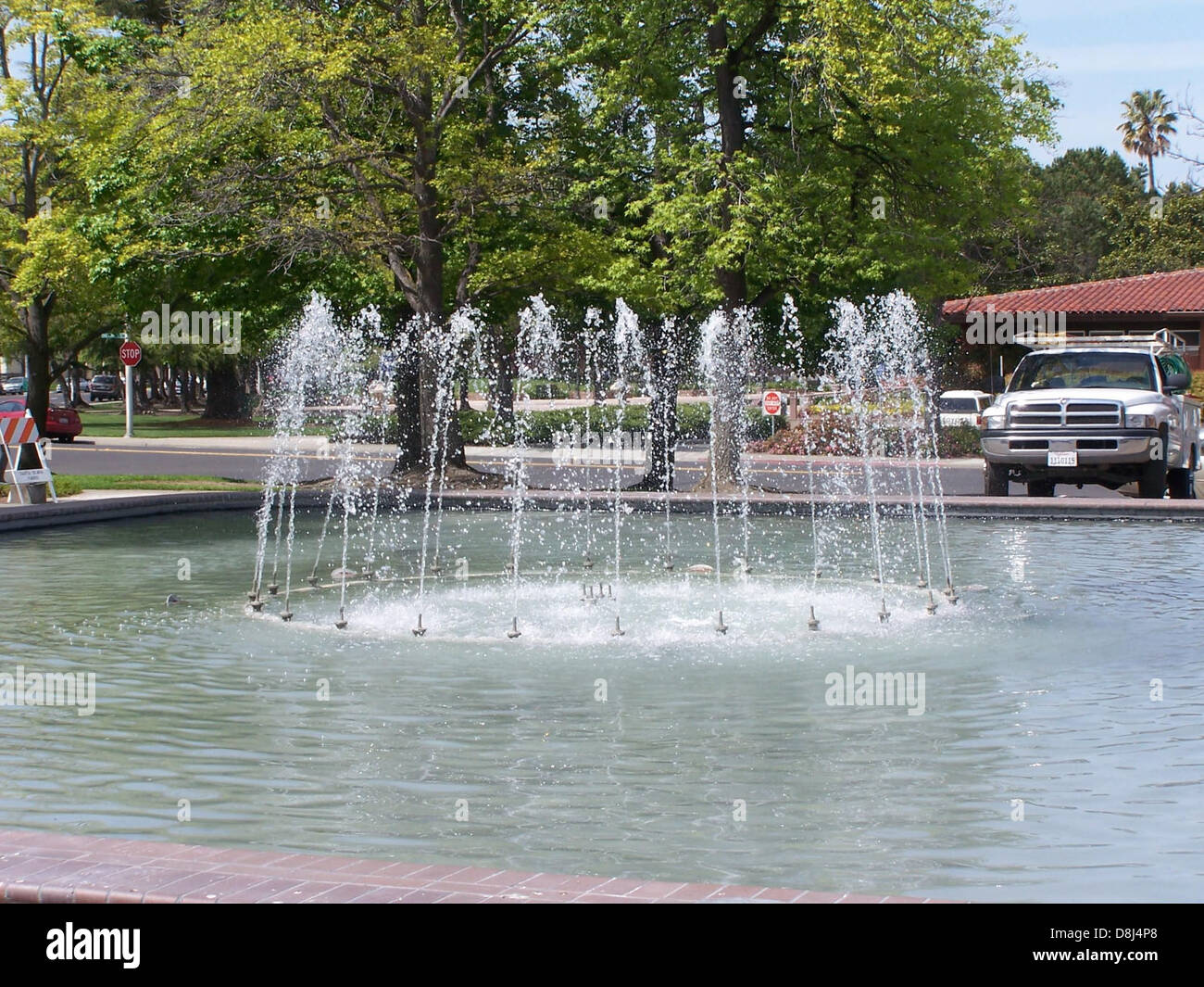 A decorative fountain in the center of a garden, with water gently flowing from the spout. The surrounding flowers and plants add to the serene atmosphere, creating a peaceful and tranquil garden environment. Stock Photo