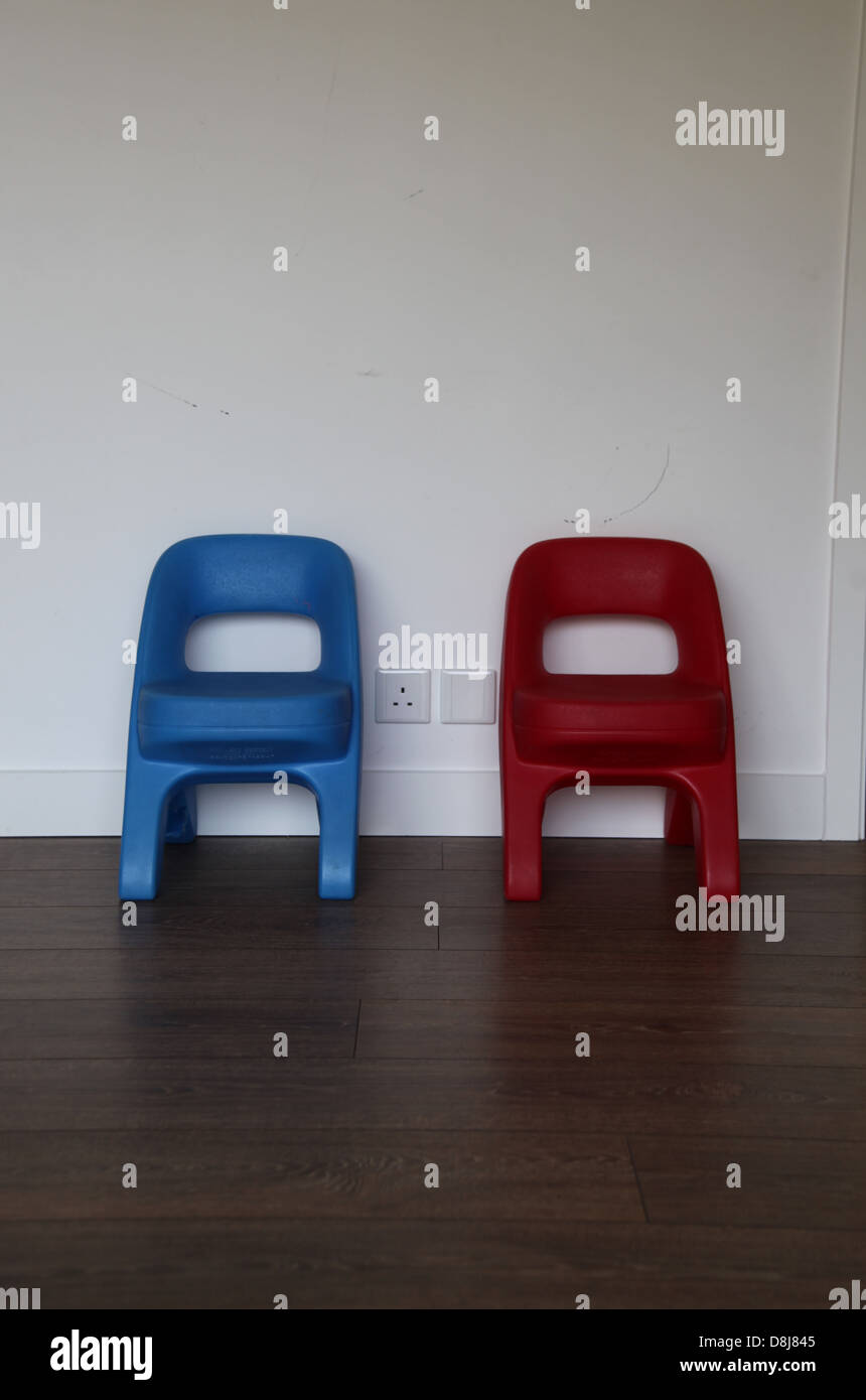 It's a photo of2 kid's chairs in plastic. one is blue, other one is red. They're side by side against a white wall. Symmetrical Stock Photo