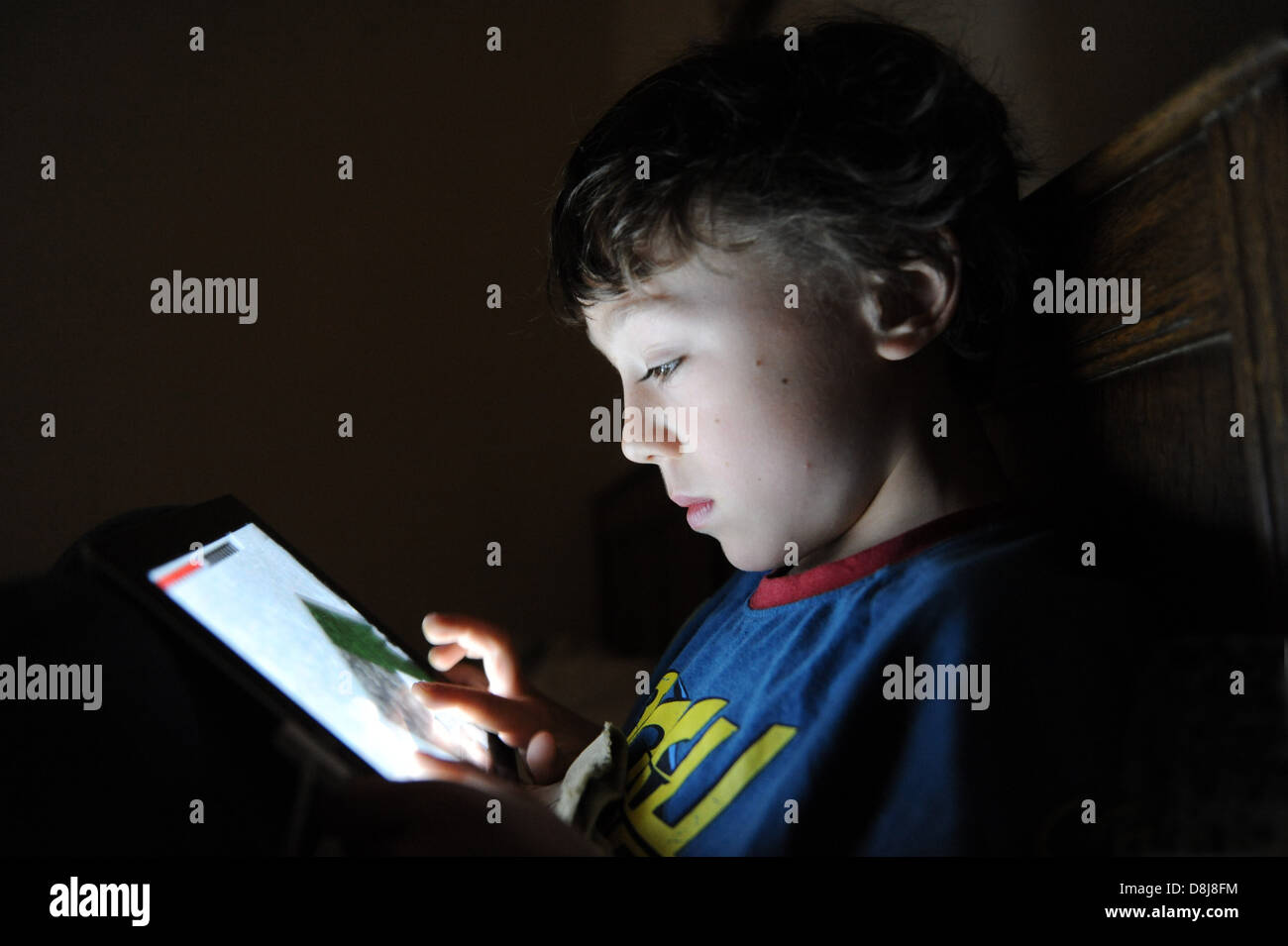 An 8 year old boy playing a computer game on his Apple IPAD in his bedroom at home. Stock Photo