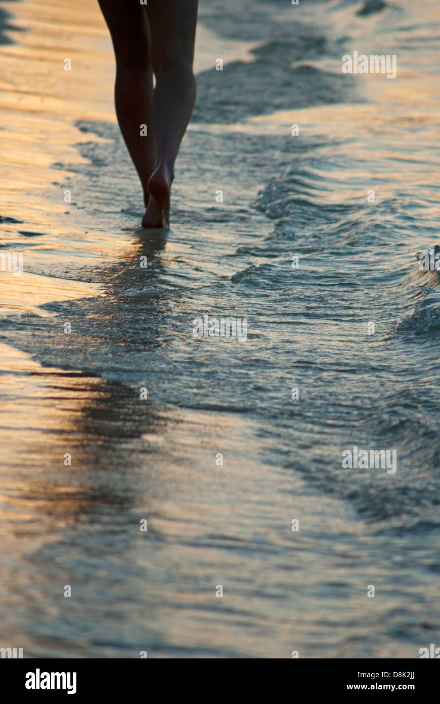 Woman walking by the edge of water on the beach Stock Photo