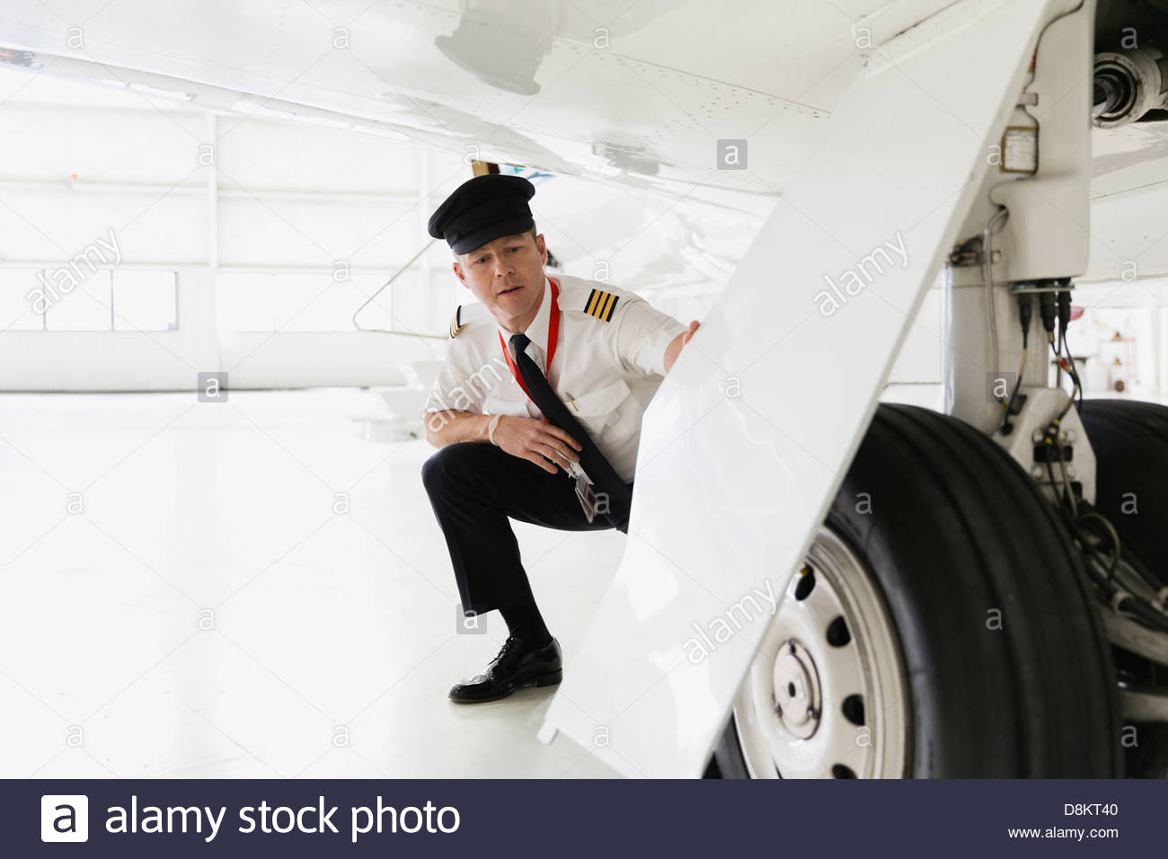 Male pilot checking airplane landing gear in hangar Stock Photo