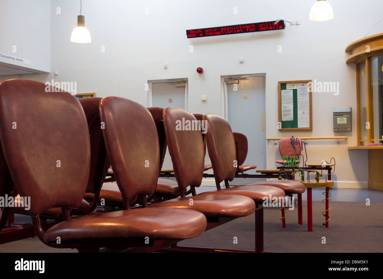 Empty seats in a doctors surgery with an electronic noticeboard advising appointments can be booked online Stock Photo