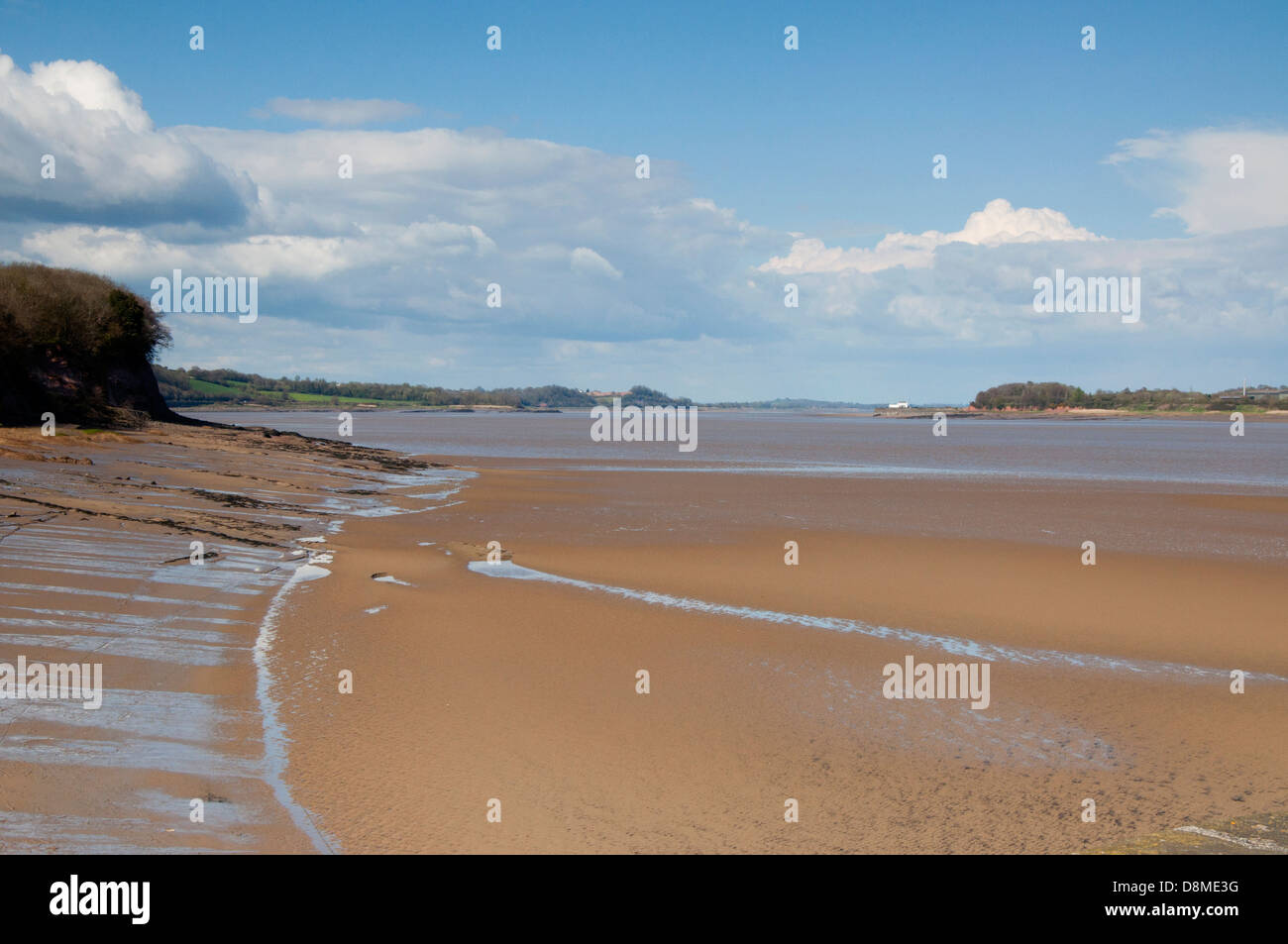 River Severn, flood defences, rocks, bank, mud, skyscape, blue sky, white and gray clouds, shrubs, trees Stock Photo