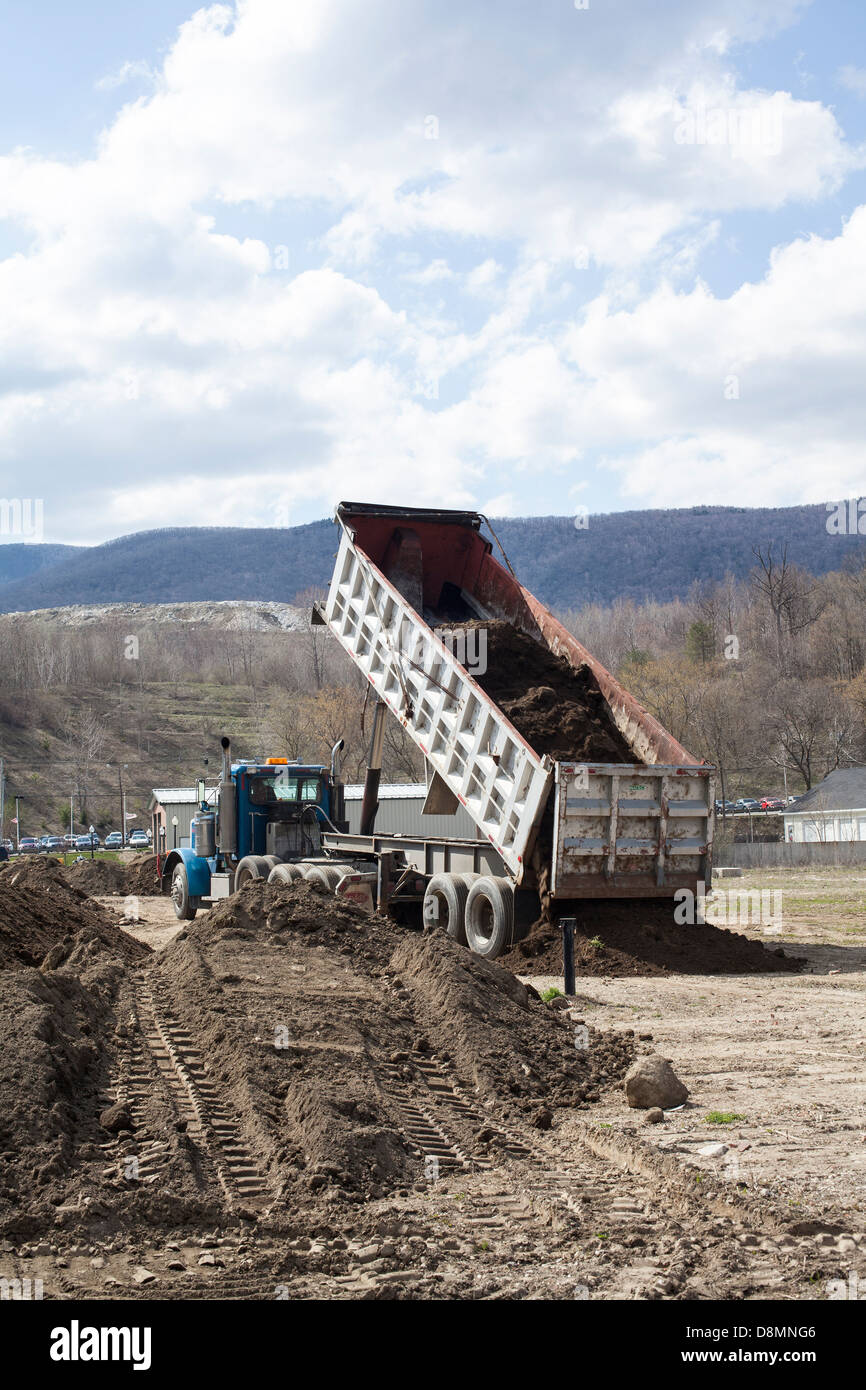 A dump truck unloads top soil by a newly constructed building in Adams