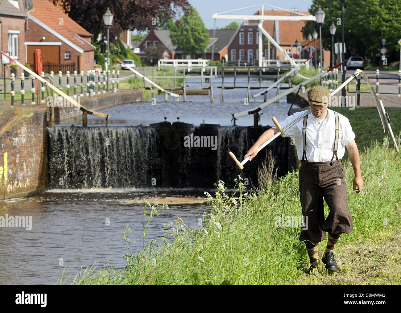 Thomas Balzen from the Fehn Museum dressed in historic clothing mows the grass in the Fehn Canal outside of the museum in Westgrossfehn, Germany, 31 May 2013. The height difference between a 17th century built channel and the natural waterway can be seen in the background. This drop was used to drive a sawmill in the past. Photo: INGO WAGNER Stock Photo