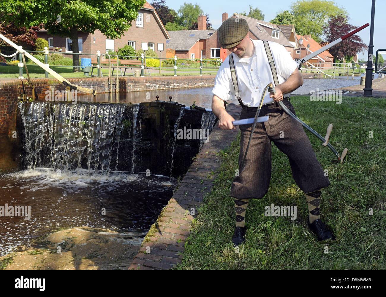 Thomas Balzen from the Fehn Museum dressed in historic clothing mows the grass in the Fehn Canal outside of the museum in Westgrossfehn, Germany, 31 May 2013. The height difference between a 17th century built channel and the natural waterway can be seen in the background. This drop was used to drive a sawmill in the past. Photo: INGO WAGNER Stock Photo
