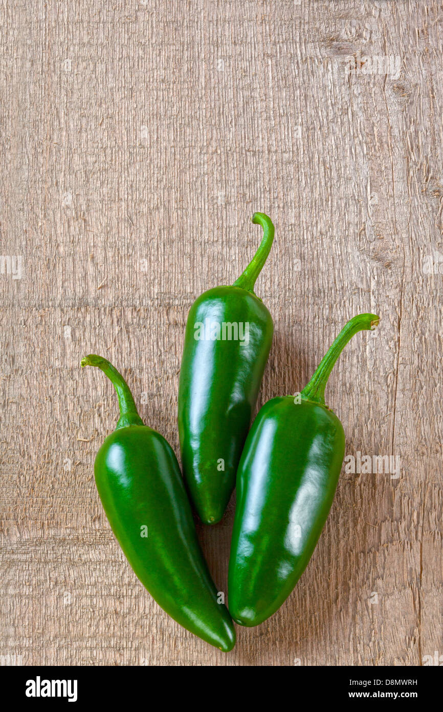 Jalapeno Chillies - three jalapeno chillies on a plank or rustic background. Stock Photo