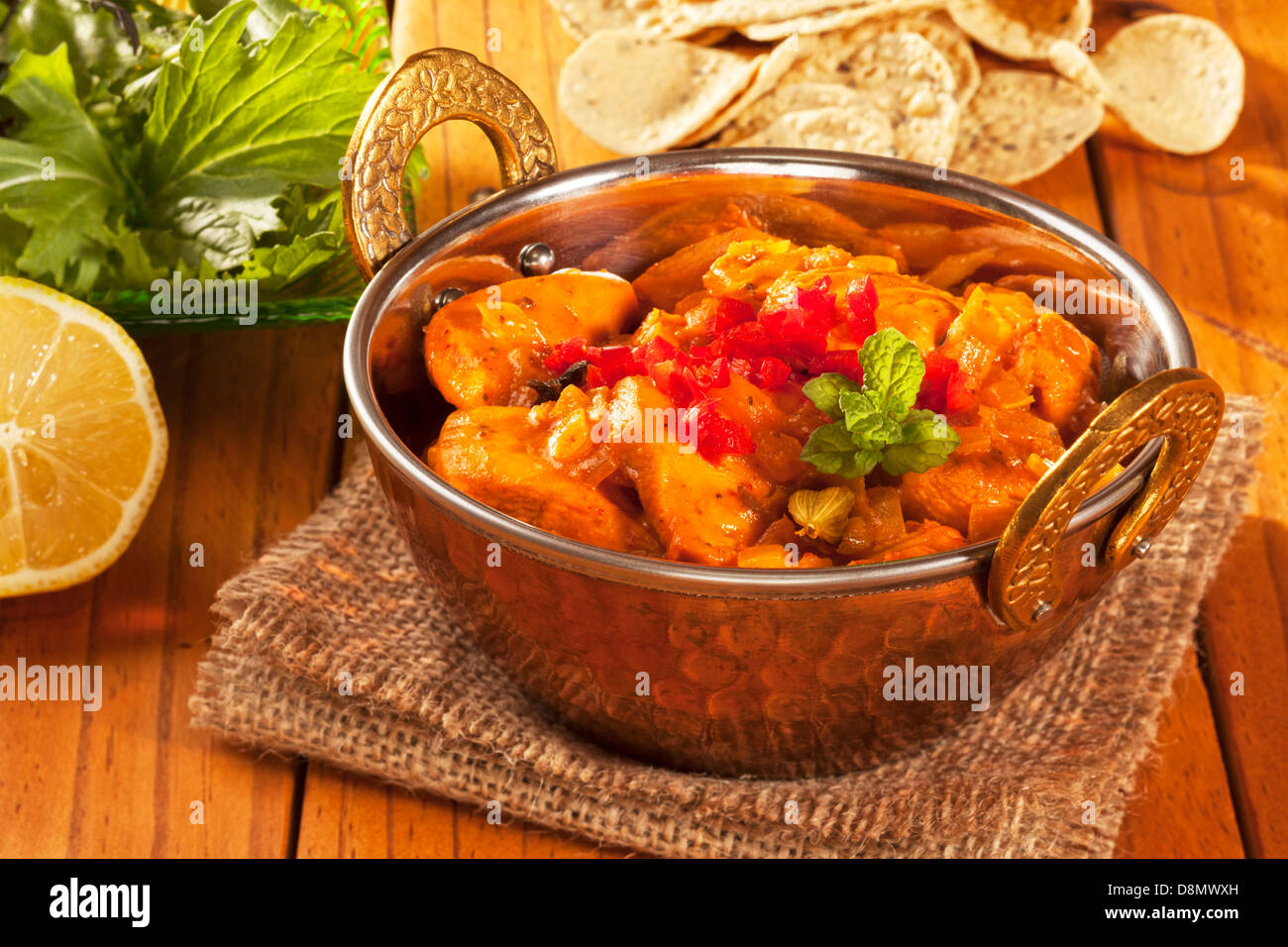 Chicken curry in a balti dish, with mini poppadums, salad and lemon. Stock Photo