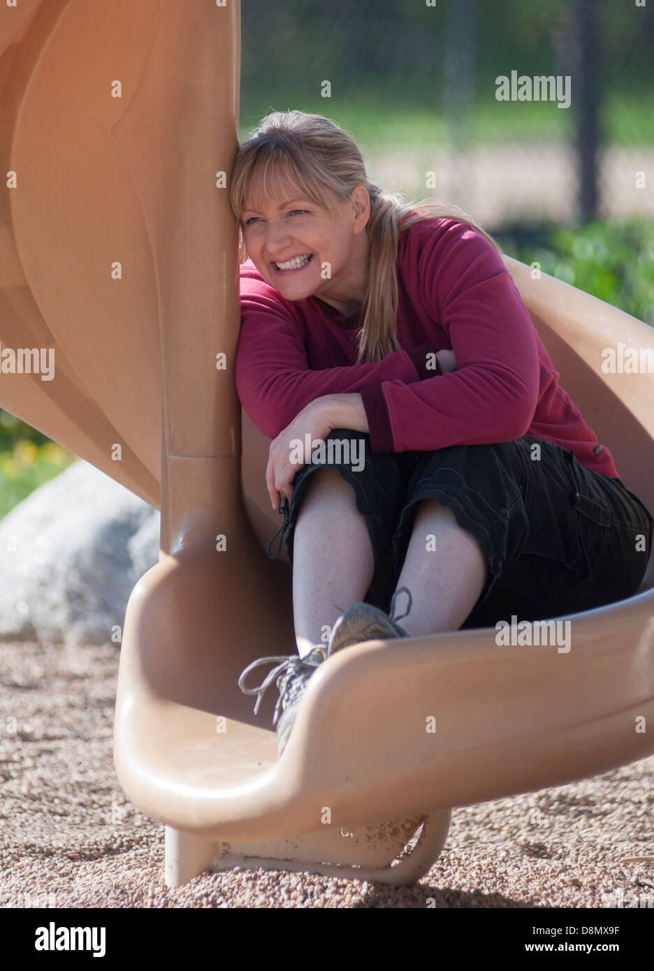 Woman with big grin sitting on outdoor slide. Stock Photo