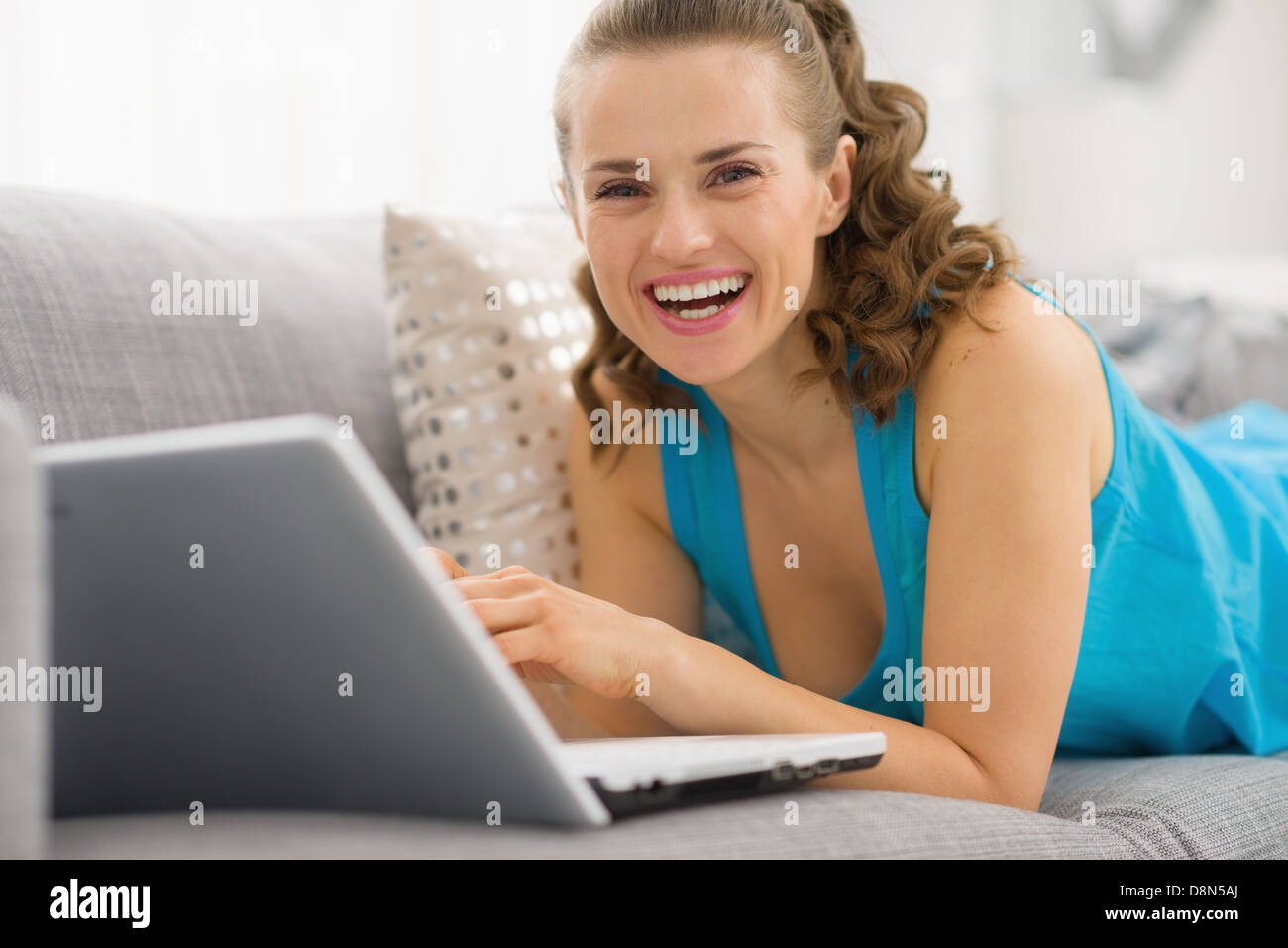 Smiling young woman laying on sofa with laptop Stock Photo - Alamy