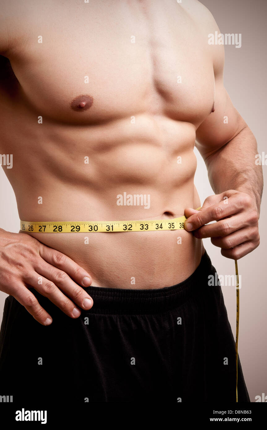 Fit man measuring his waist after a workout in the gym, in a dark brown background Stock Photo