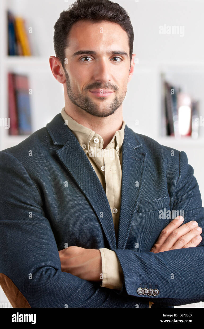 Casual businessman with arms crossed with a bookshelf behind him Stock Photo