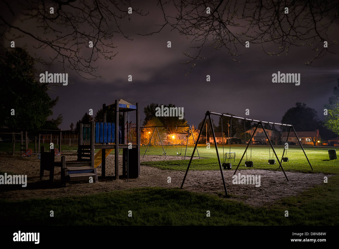 A creepy scene of a deserted children's playground in a suburban park at night time. Stock Photo