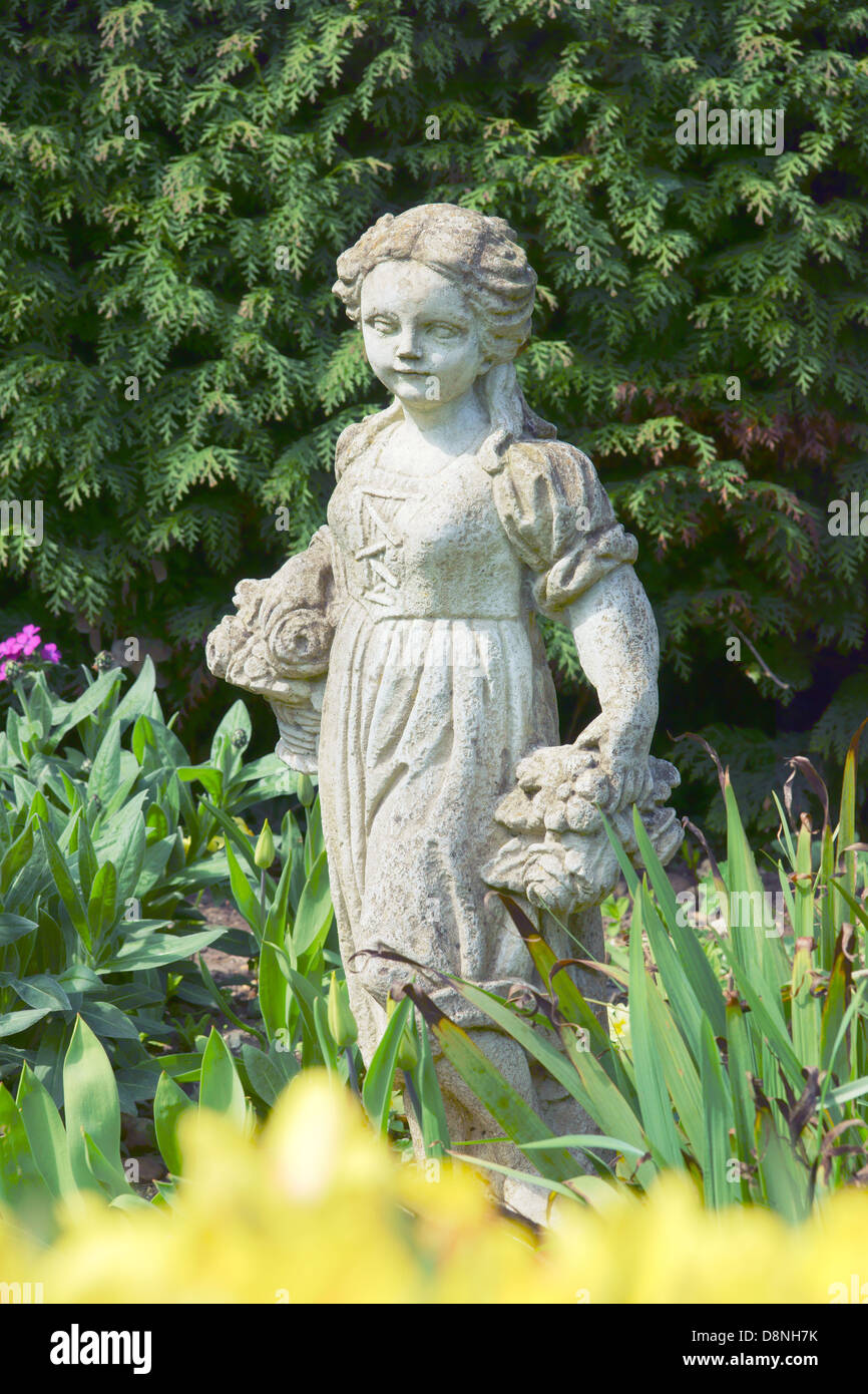 A garden ornament. Statue of a young girl carrying two bunches of