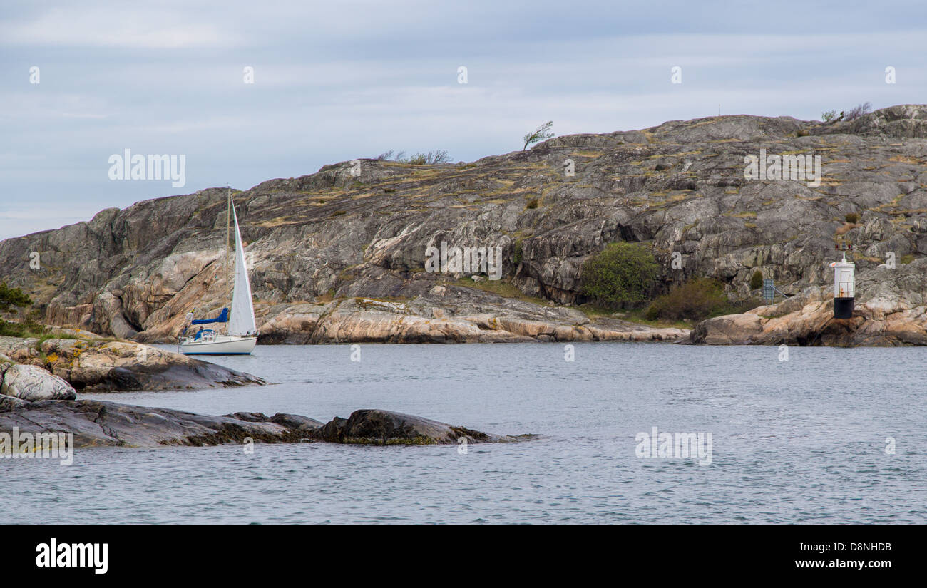 A sail boat sailing between rocky islands in Styrsö, an archipelago