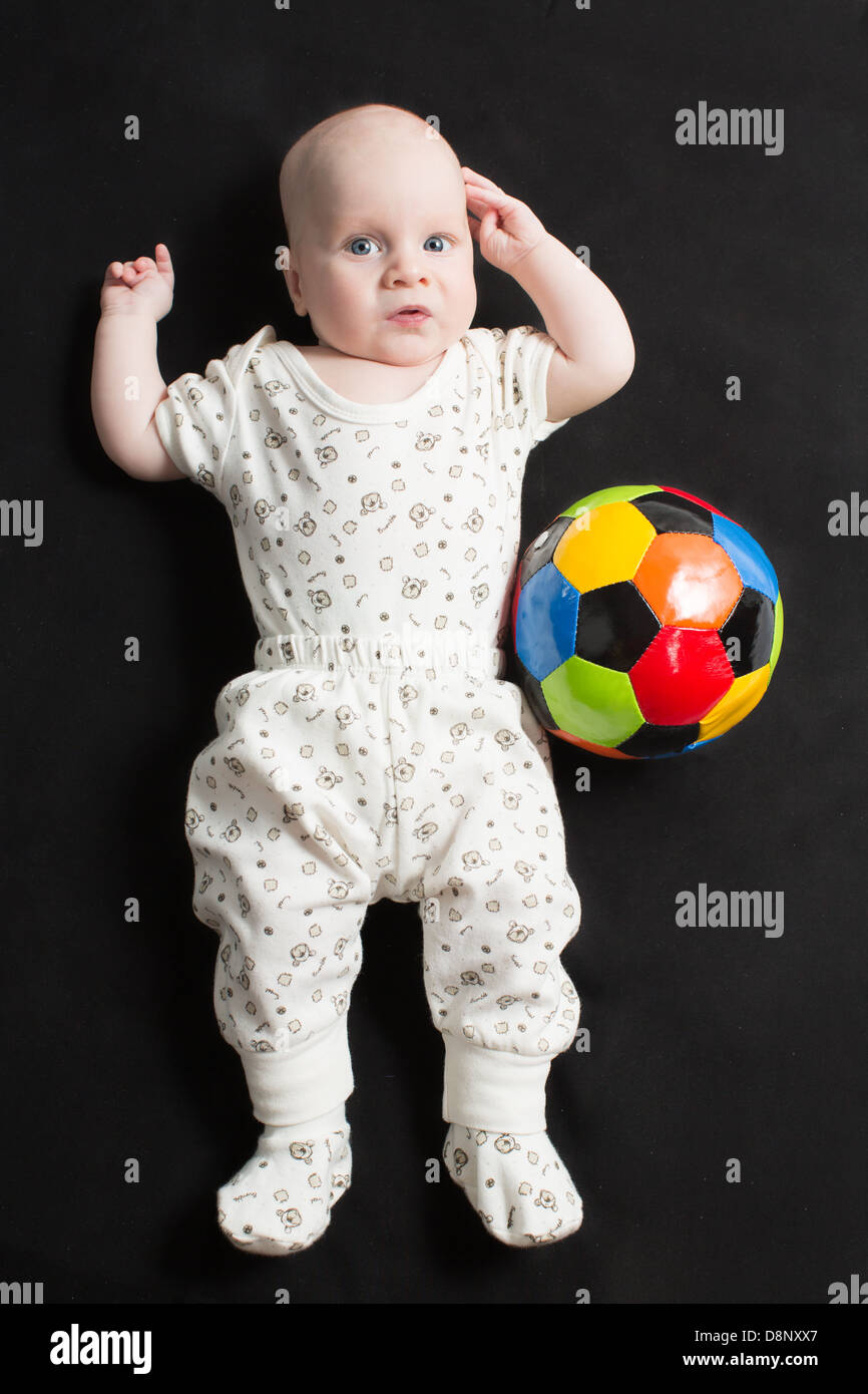 Baby boy playing with a soccer ball on black background. Babies And