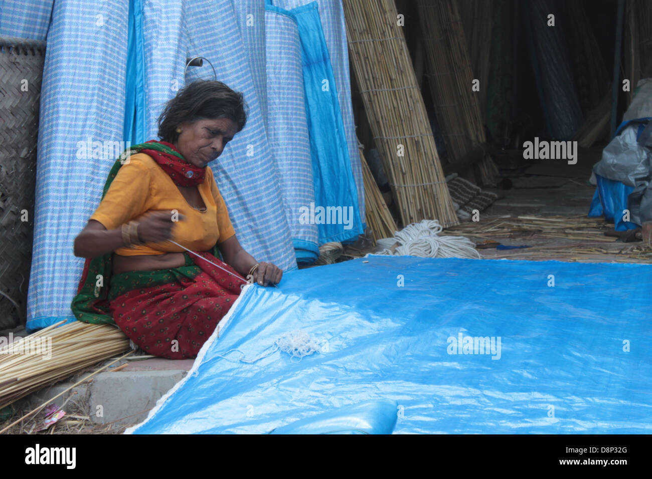 A woman stitches a bamboo-curtain in Delhi, India. Stock Photo