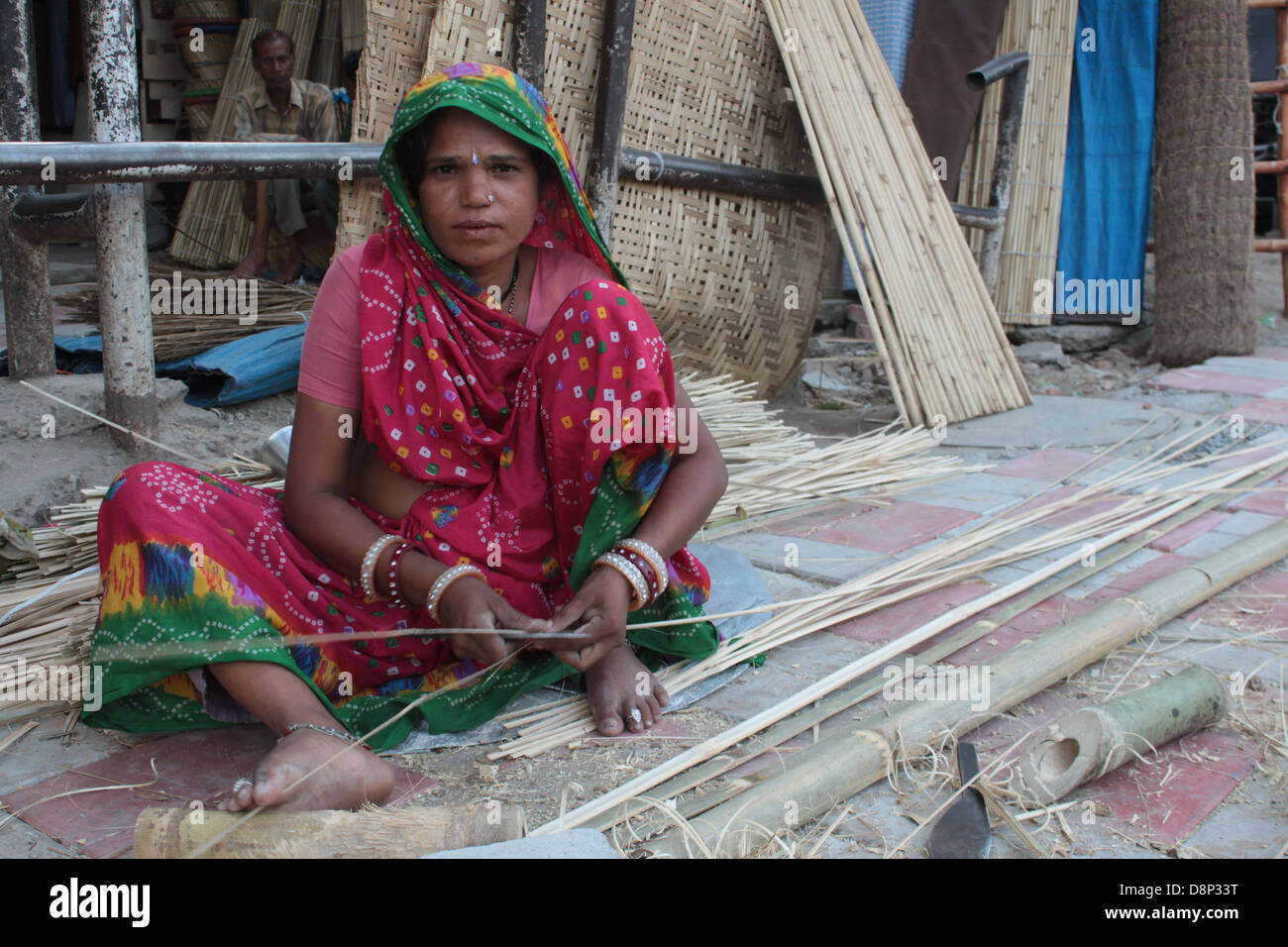 A woman worker slits bamboos to make curtains on a pavement in Old Delhi, India. Stock Photo