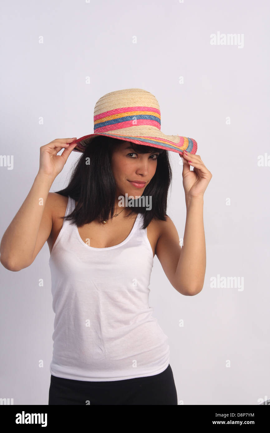 Pretty, young Latino woman playing with a striped straw hat on her head. Stock Photo
