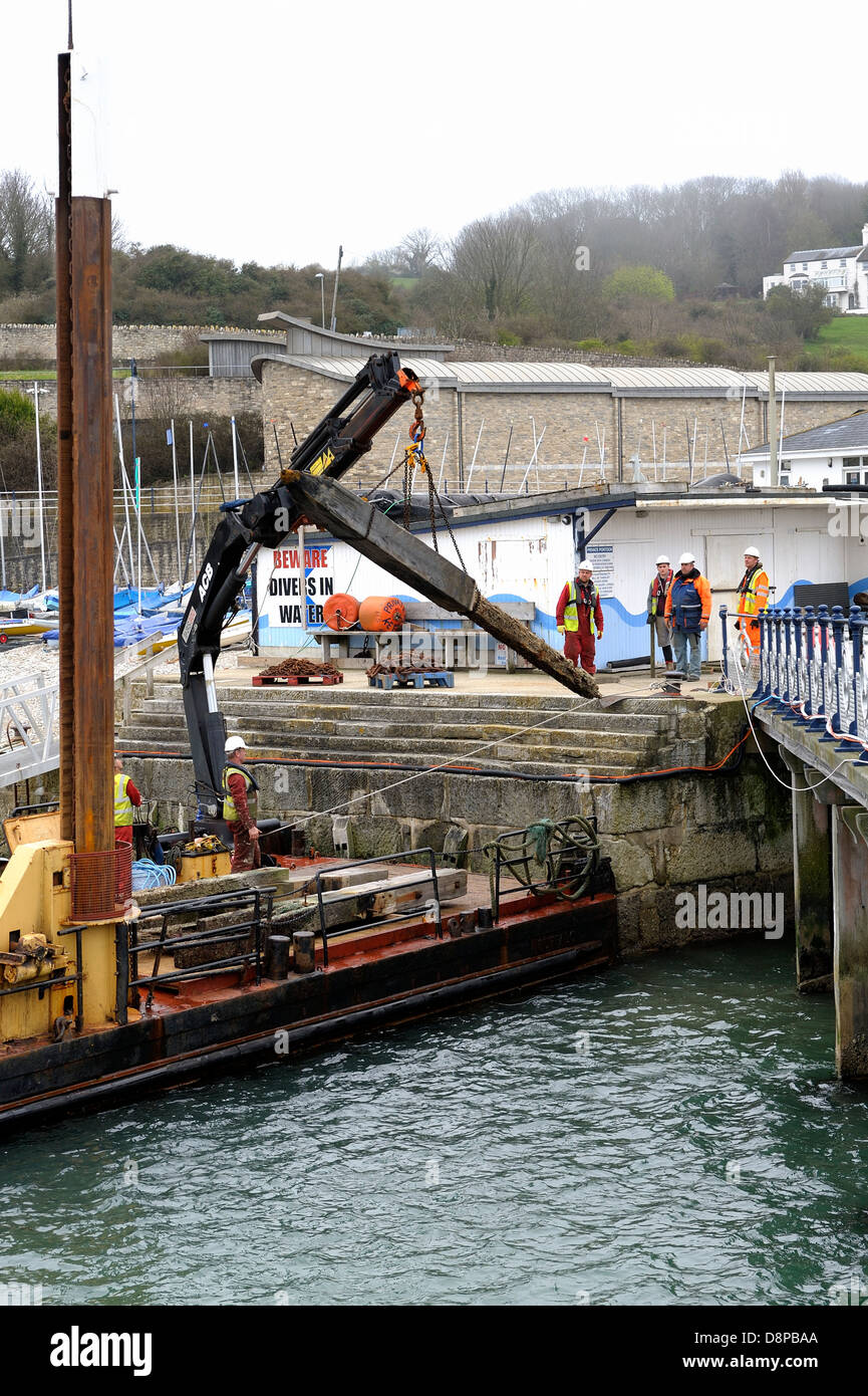 rotting pier timber piles being dropped onto the quayside using BUFFALO by contractors jenkins marine Dorset Engand uk Stock Photo