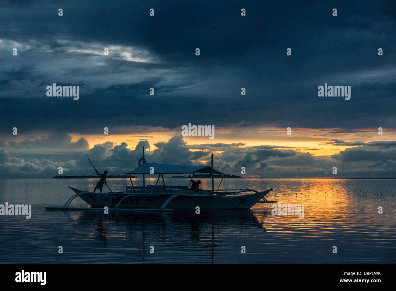 Boy pushing a bangka boat - a traditional Filipino fishing boat - with a long pole in sunset Stock Photo