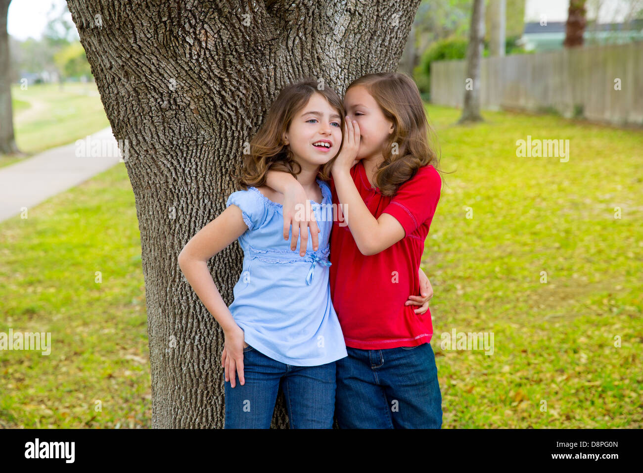 children kid friend girls whispering ear playing smiling in a park tree outdoor Stock Photo