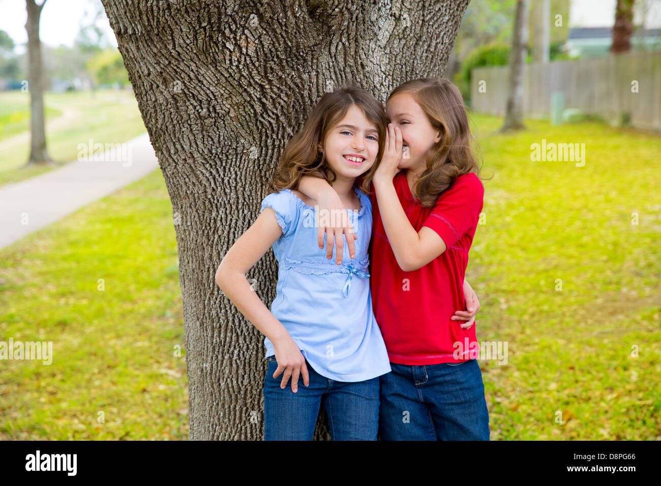 children kid friend girls whispering ear playing smiling in a park tree outdoor Stock Photo