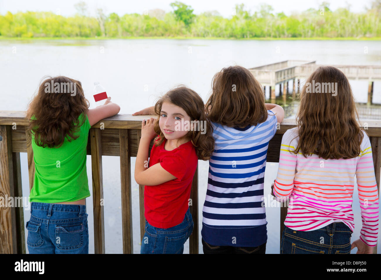 Children girls rear view looking at lake on railing and one looking ...