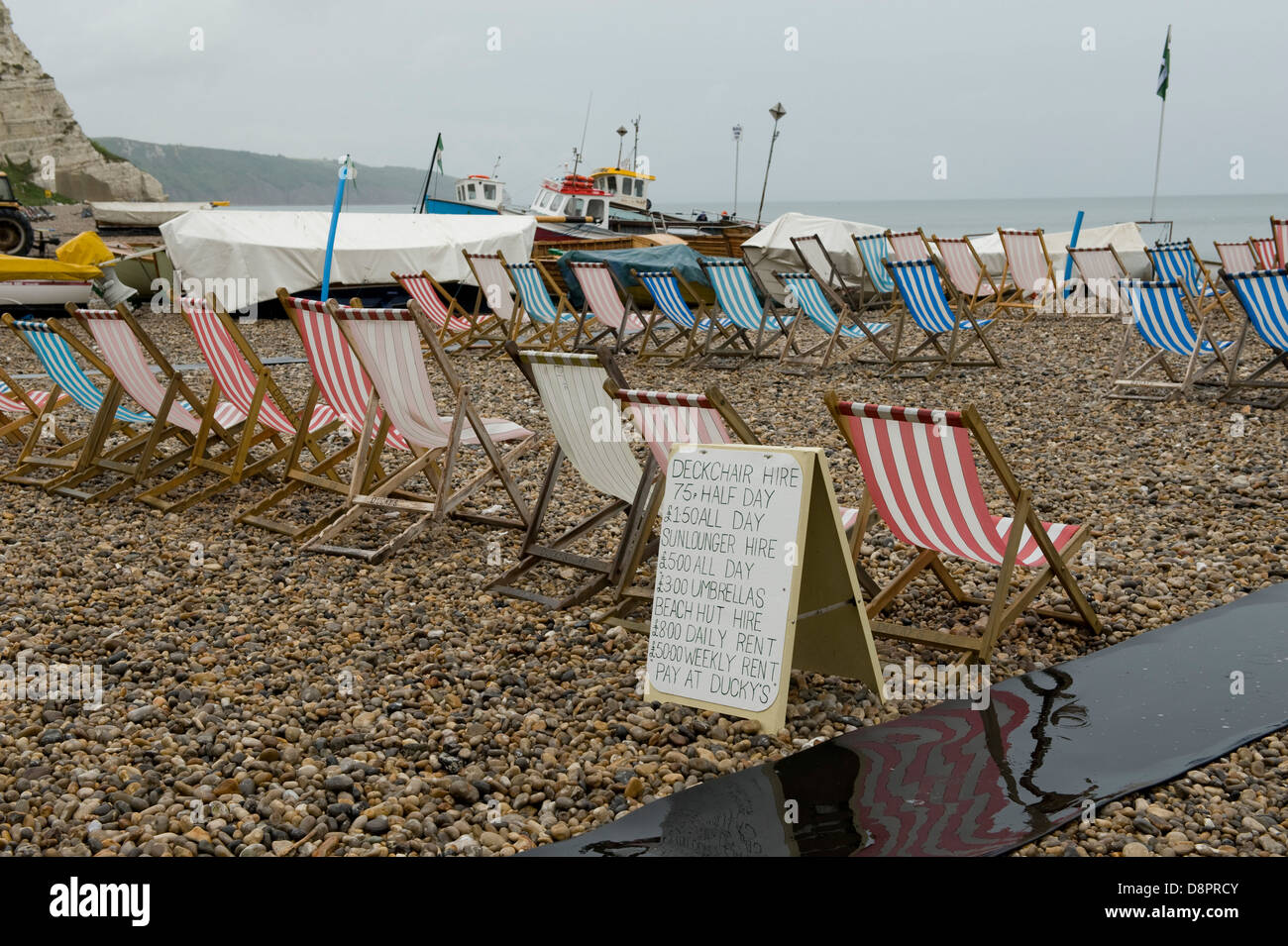 Unoccupied deck chairs and notice on a wet summer day at Beer Beach in