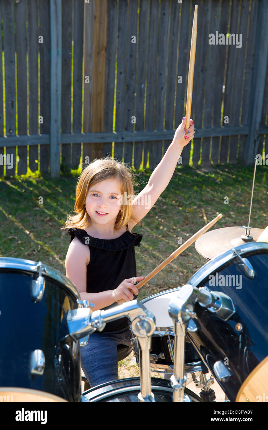 Drummer blond kid girl playing drums in tha backyard lawn Stock Photo