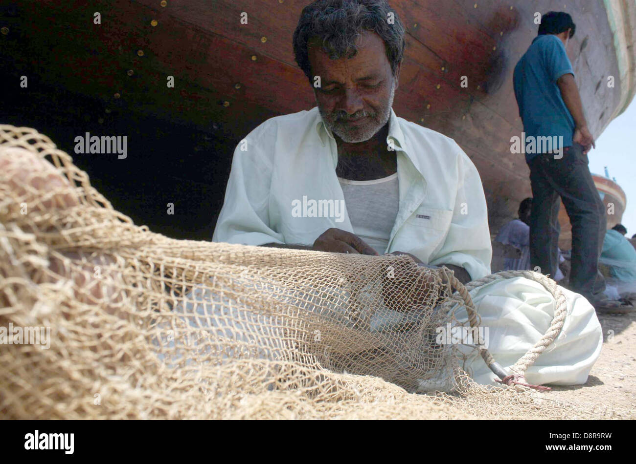 Man busy in knitting fish catching net to earn his livelihood for support  his family, on other hand fishing is ban due to rough sea, at Fishery in  Ibrahim Hyderi in Karachi