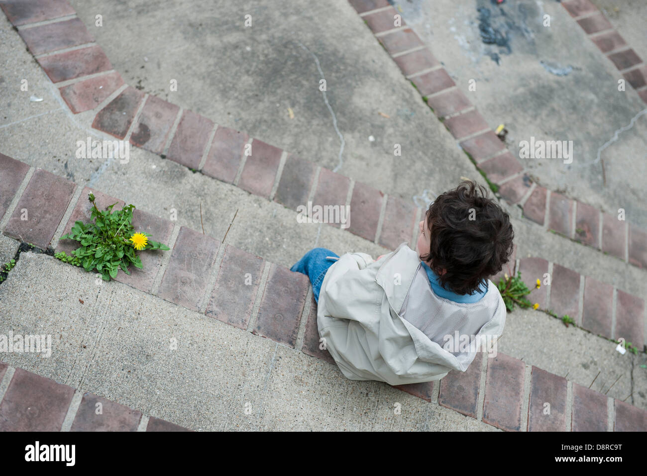 Boy sitting alone on steps, looking away in thought Stock Photo