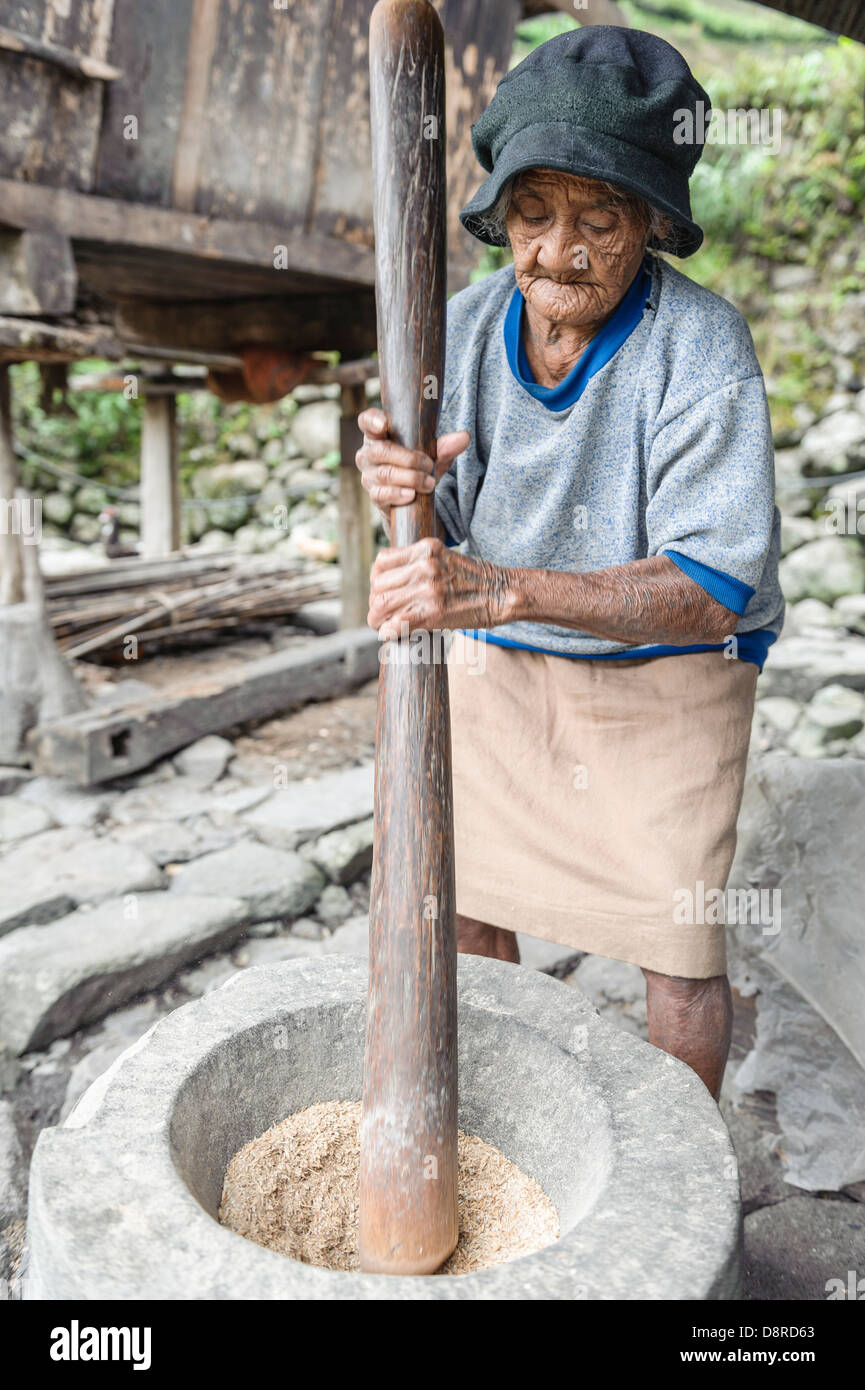 Woman pounding rice in a rural village, Batad, Luzon, Philippines Stock Photo