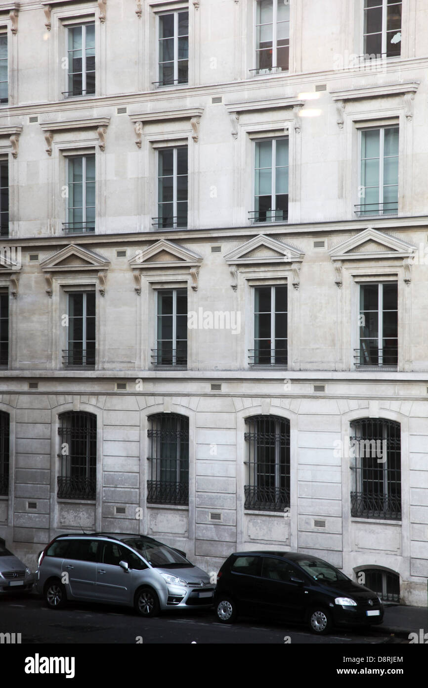 It's a photo of the front of a Typical Parisian Building in Paris, France. We see the street with 3 cars that are parked. Nobody Stock Photo