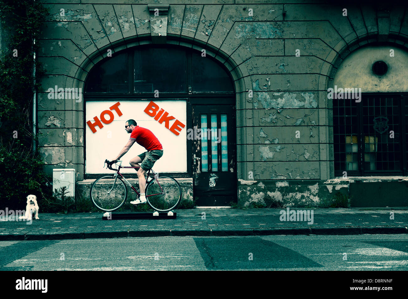 Cyclist on racing cycle training on a role in front of a rundown builing. Stock Photo