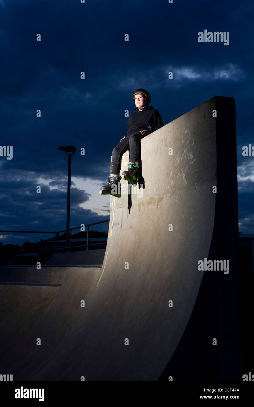 A young inline skater siting on top of a high concrete wall in a skate park. Stock Photo