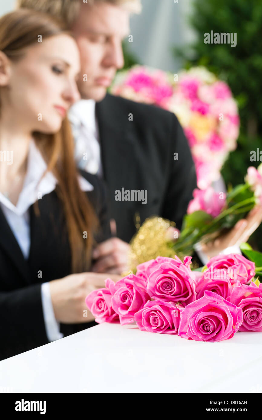 Mourning man and woman on funeral with pink rose standing at casket or coffin Stock Photo