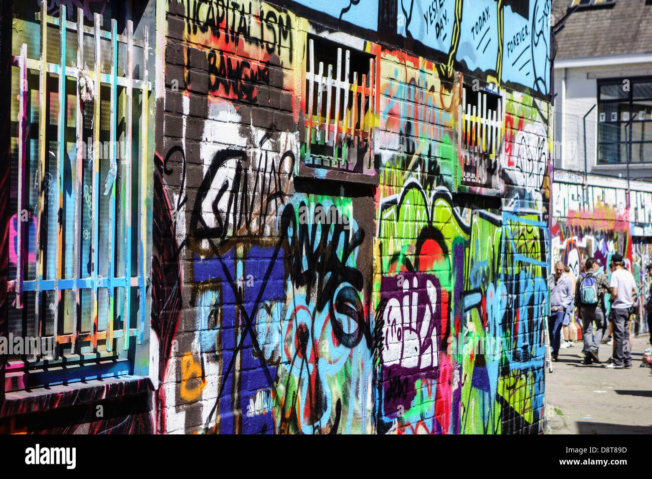 Youngsters in alley spraying colourful graffiti on wall of building in city Stock Photo