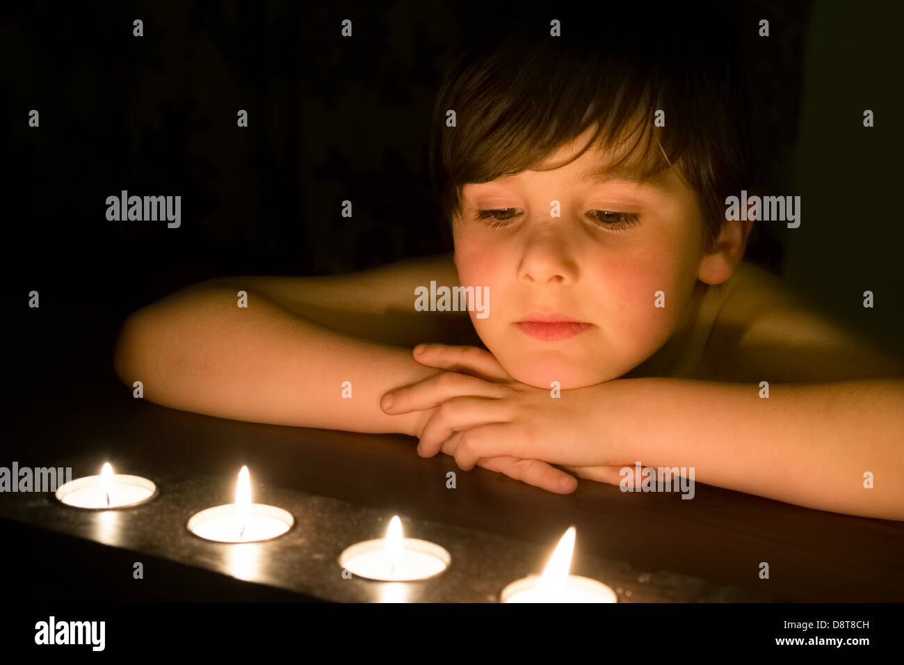 A male Caucasian child stares at lit tea light candles Stock Photo
