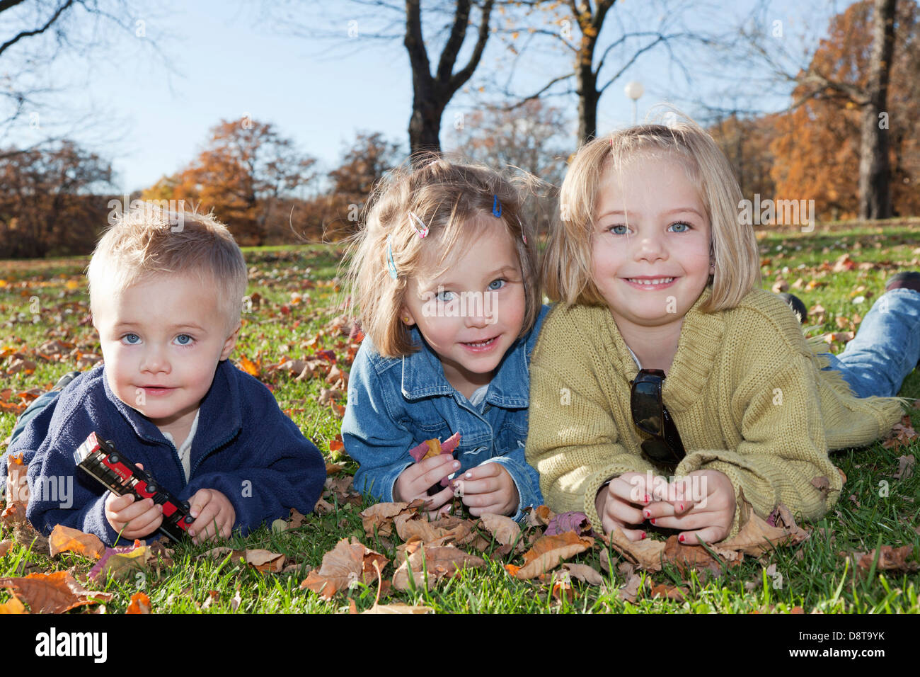 Two year-old boy with his sisters, six and four year-old, in autumn in a park Stock Photo