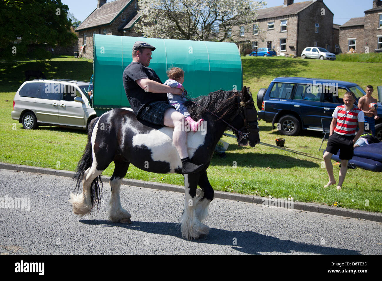 Gypsy travellers in Bainbridge, Richmondshire, North Yorkshire, UK June, 2013. Father and cvhild on horseback as members of the travelling community travel en-route to the Appleby Horse Fair in Cumbria.  The Fair is an annual gathering of Gypsies and Travellers which takes place on the first week in June, and has taken place since the reign of James II, who granted a Royal charter in 1685 allowing a horse fair 'near to the River Eden'. Stock Photo