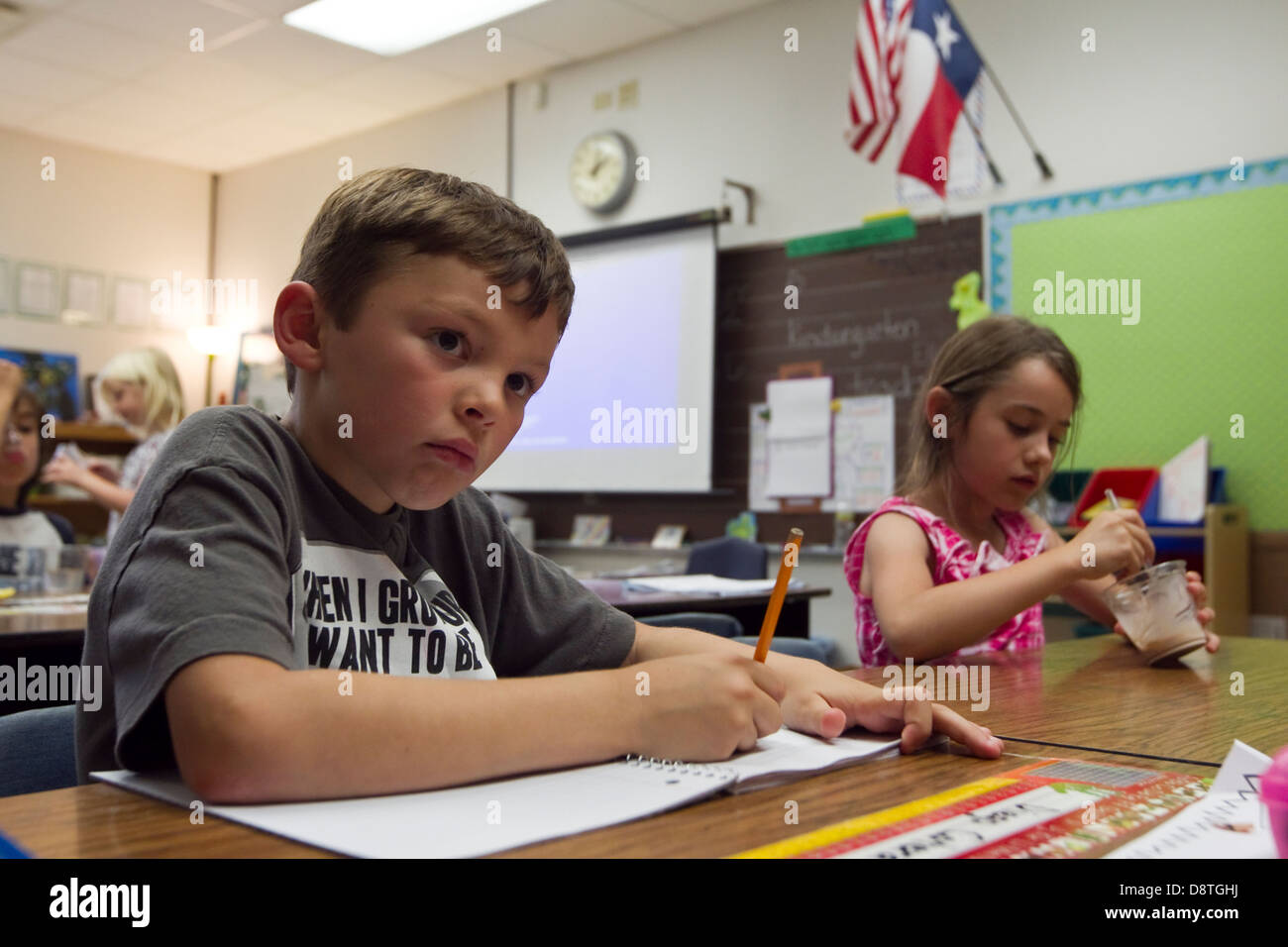 7 year old Mexican-American boy sits in first grade elementary school  classroom and writes in notebook with a pencil Stock Photo