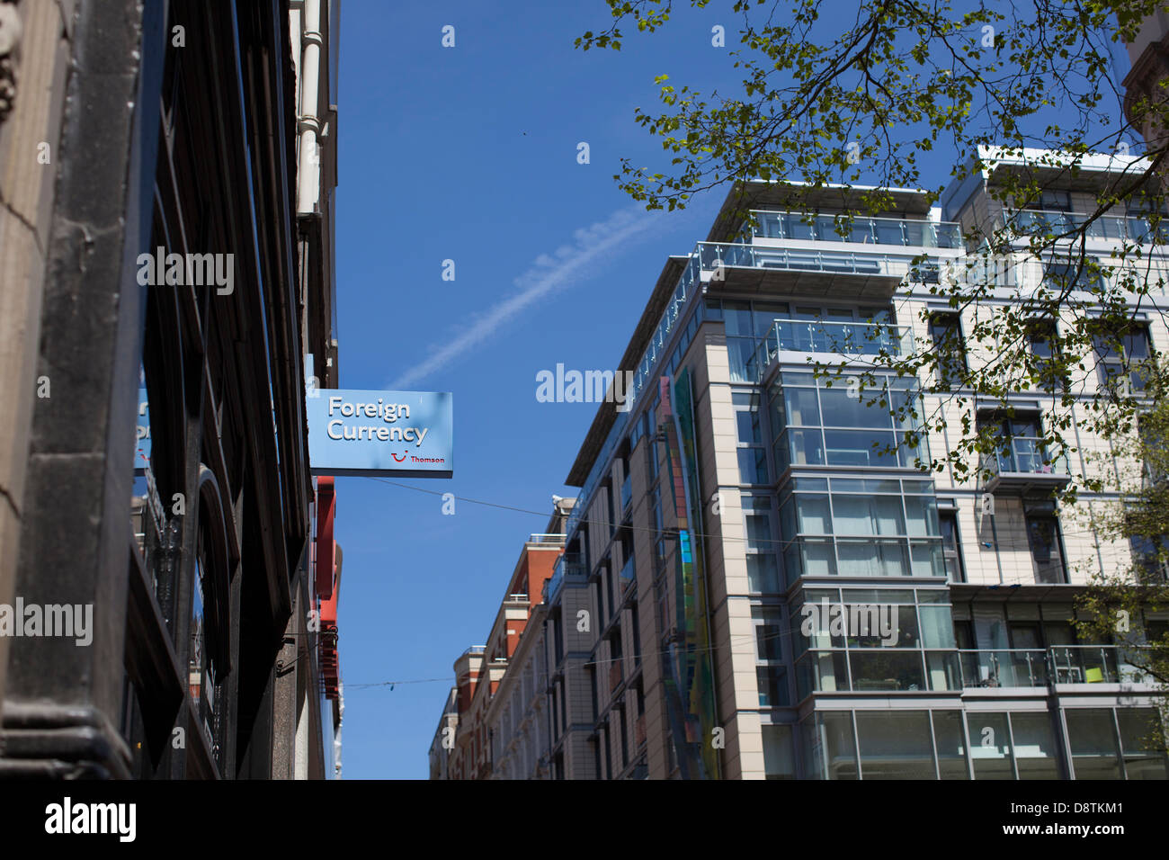 A Thomson foreign currency sign against a blue sky with a holiday jet vapour trail in a city centre in the UK Stock Photo